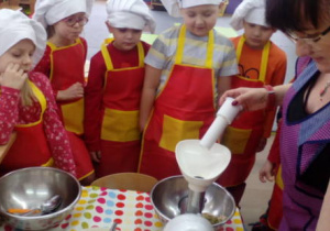 Dzieci w strojach kucharzy obserwują pracę czynność mielenia składników z użyciem maszynki